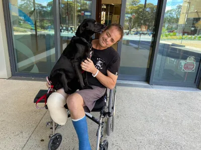Tim in a wheelchair just out of hospital, hugging his dog Maisey