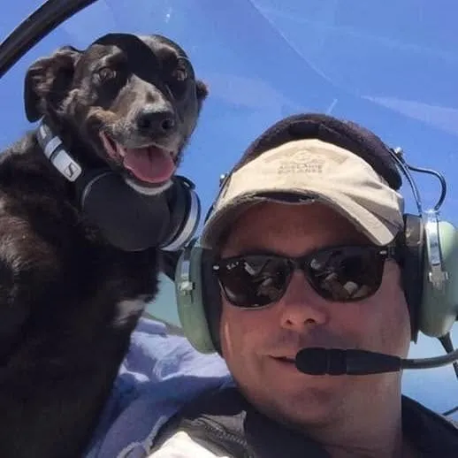 Tim flying a light plane with his black dog in a headset beside him